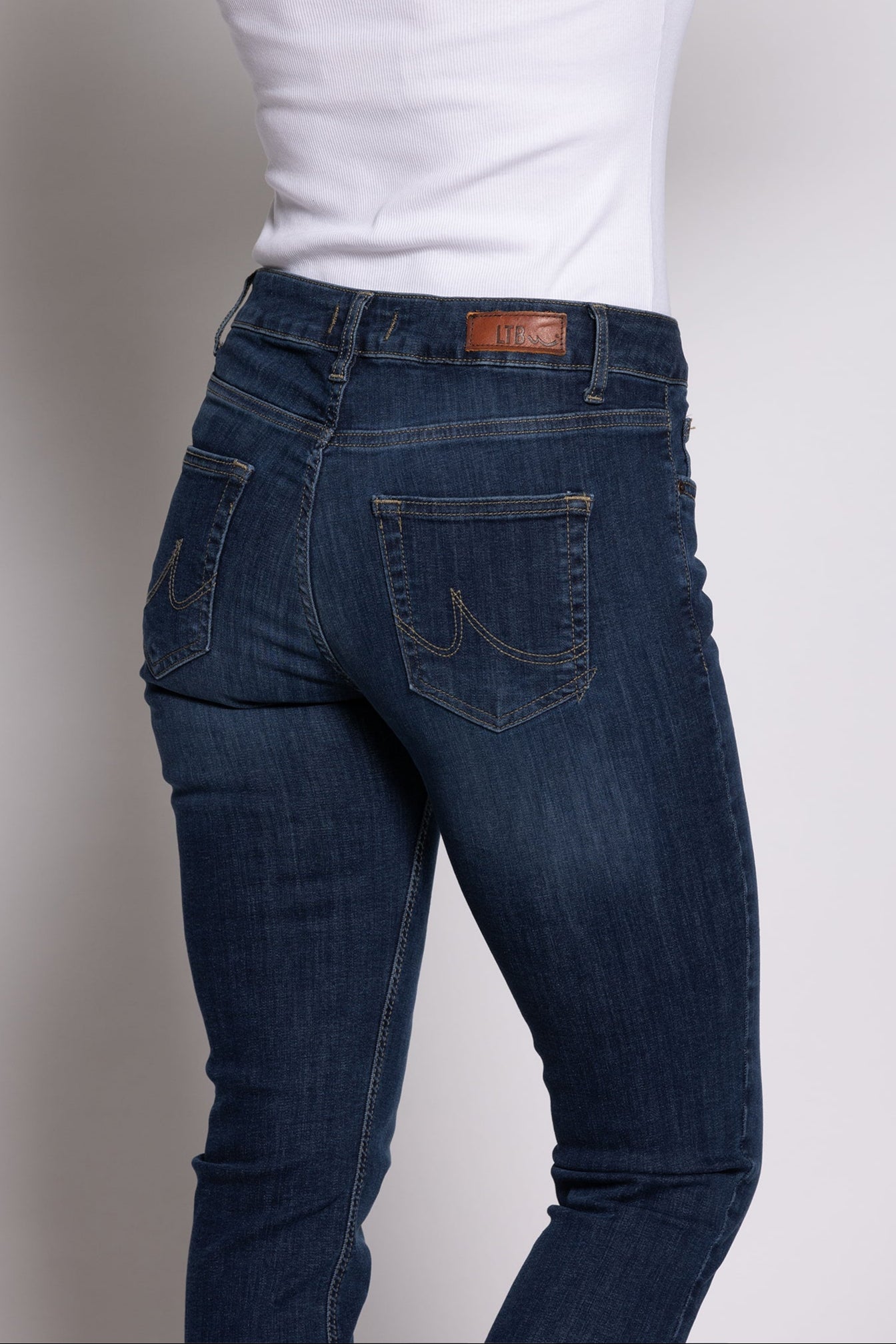 Women wearing blue jeans and a white shirt against a plain background