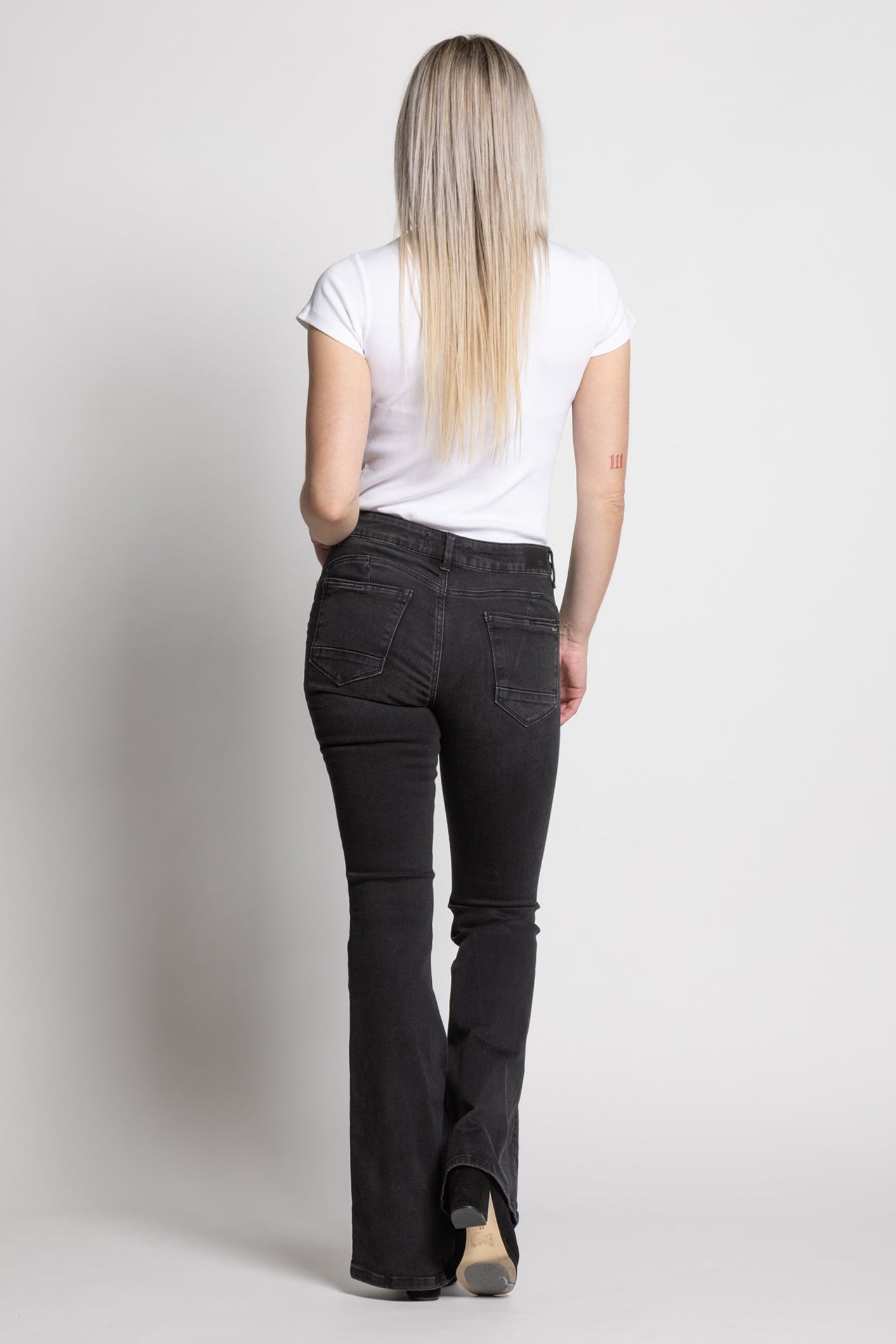 Woman wearing black flared jeans and a white t-shirt on a plain background