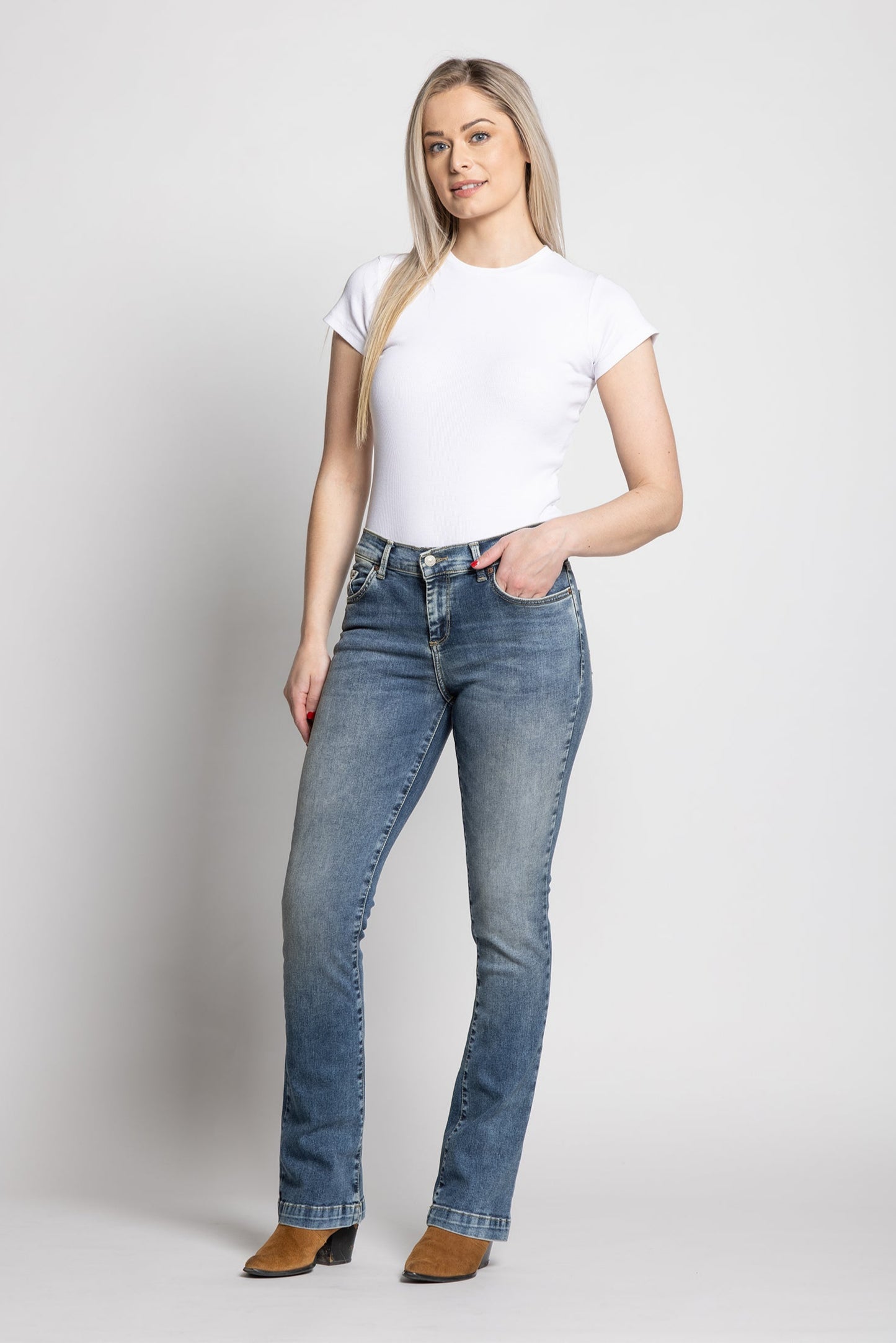 Woman wearing a white t-shirt and blue jeans on a plain background