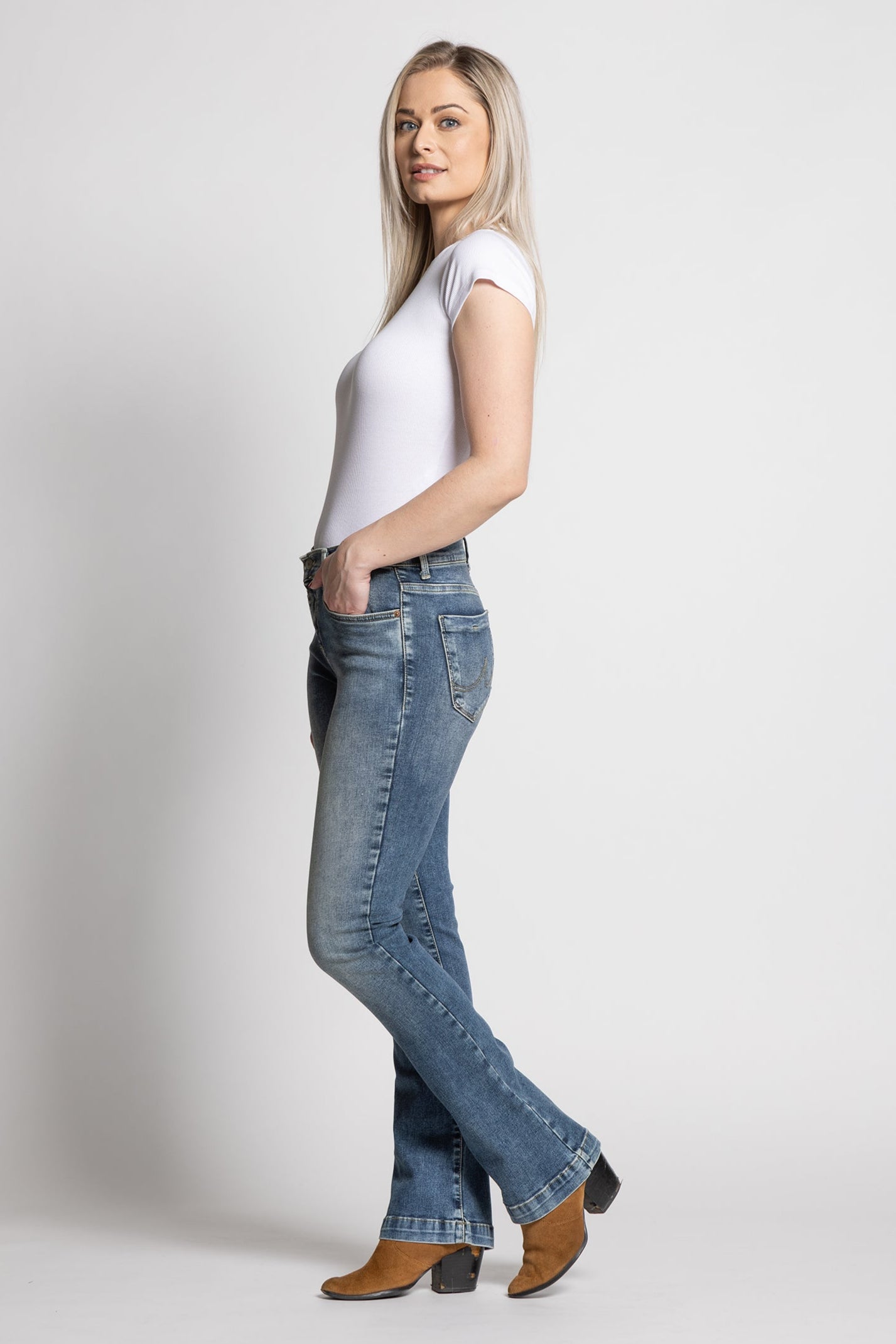 Woman wearing a white t-shirt and blue jeans on a plain background