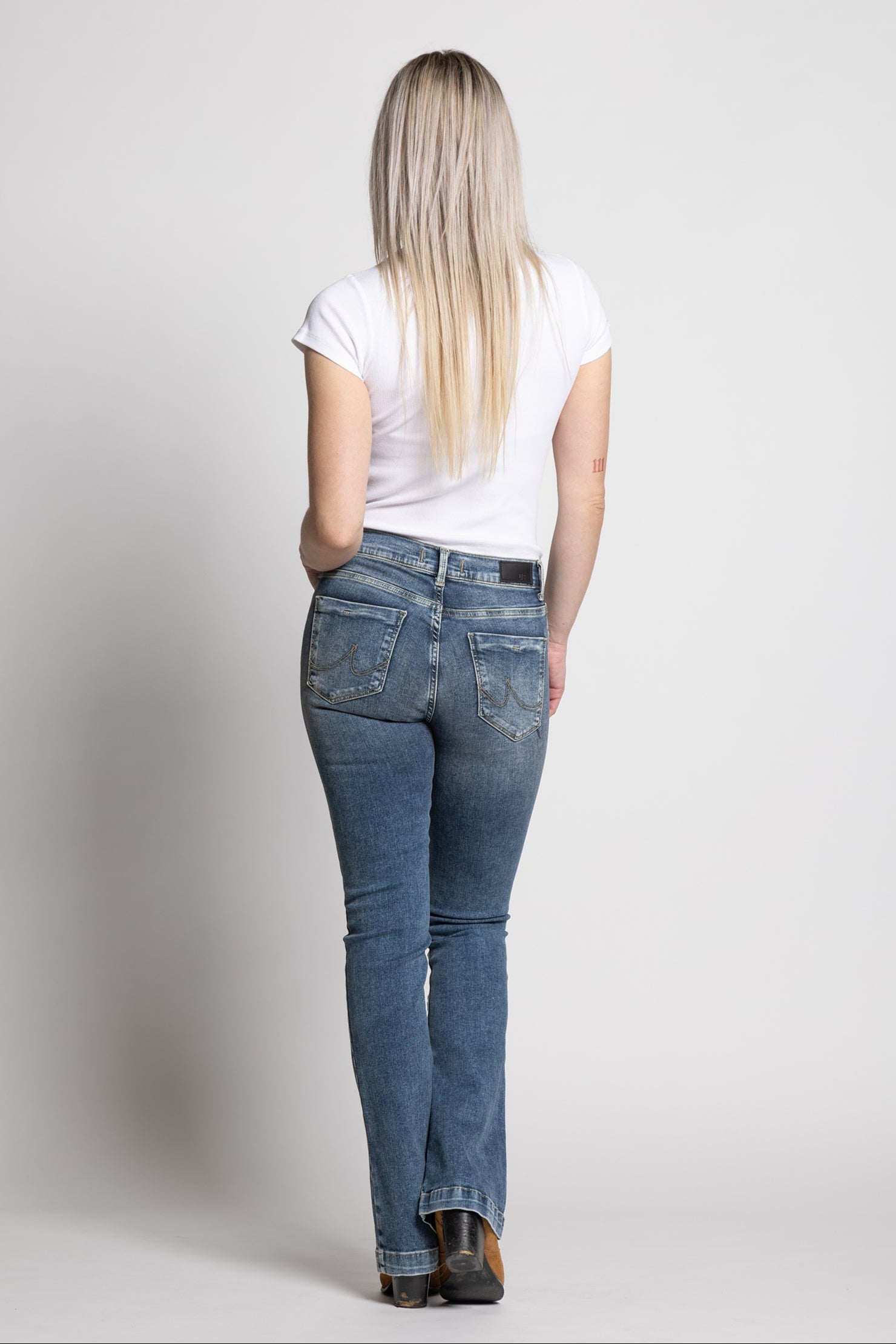Woman wearing blue jeans and a white t-shirt on a plain background