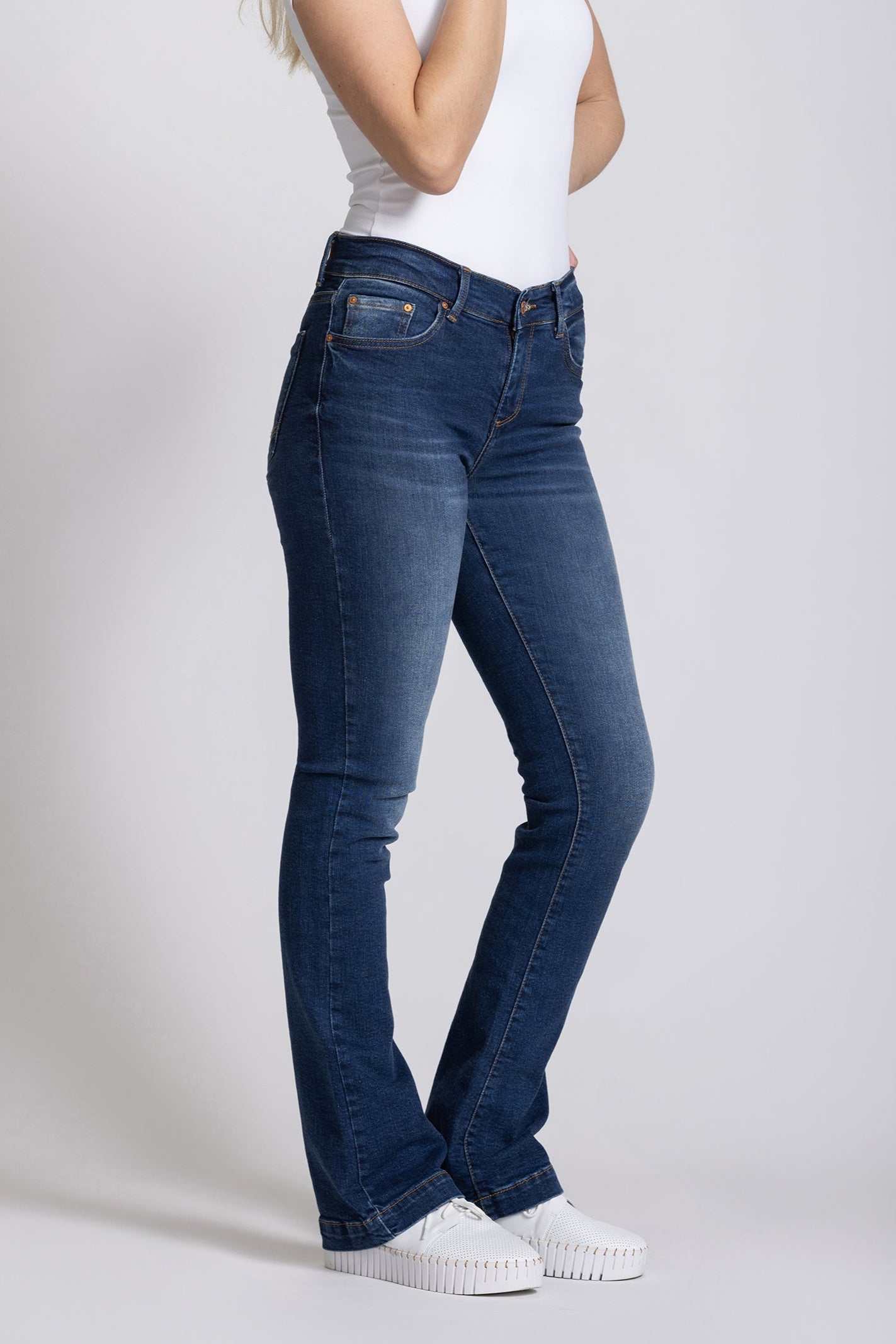 Woman wearing blue jeans and a white t-shirt on a plain background