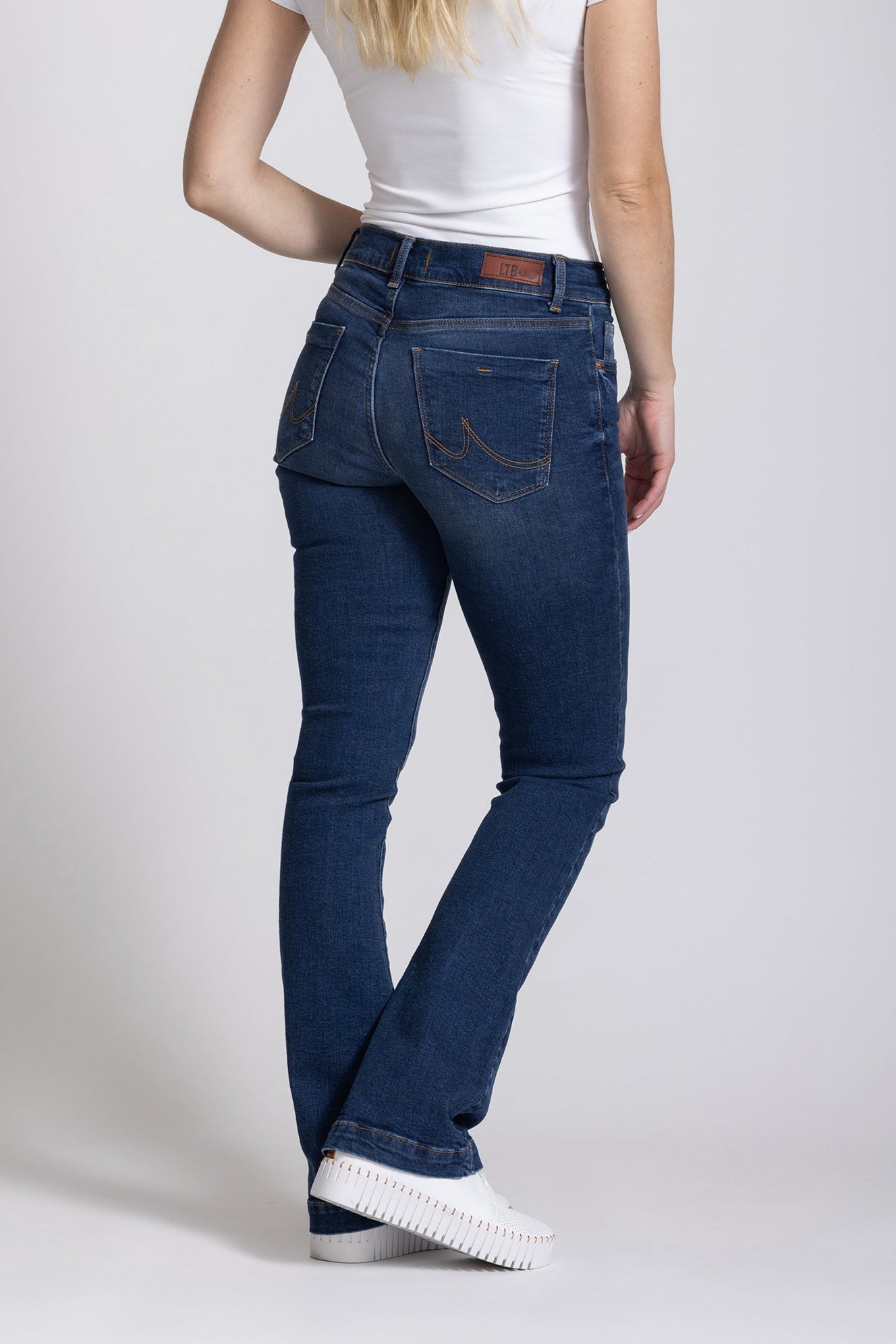 Woman wearing blue jeans and a white shirt on a plain background