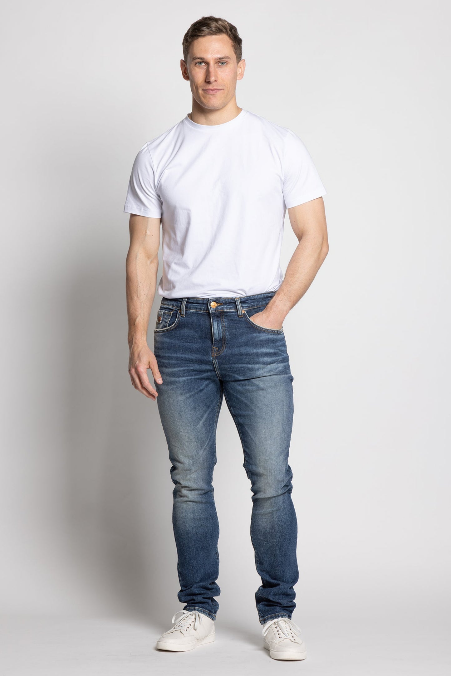 Man wearing a white t-shirt and blue jeans on a plain background