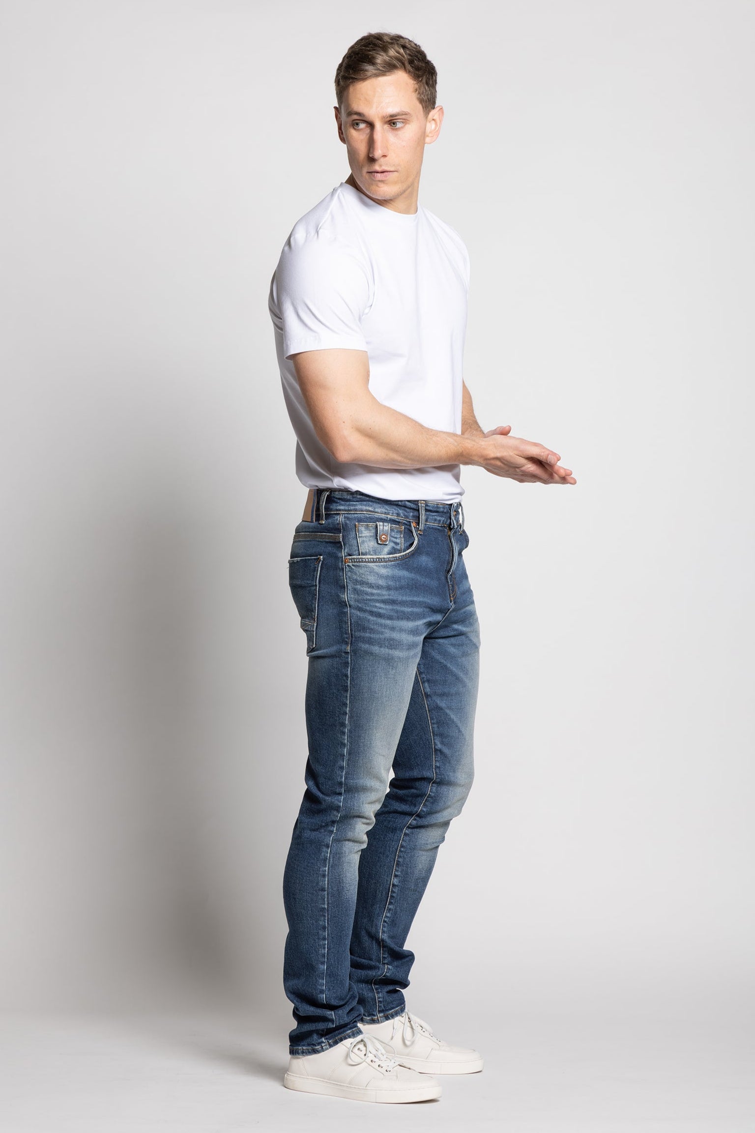 Man wearing a white t-shirt and blue jeans on a plain background