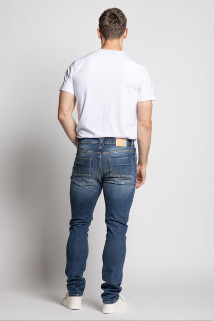 Man wearing a white t-shirt and blue jeans on a plain background
