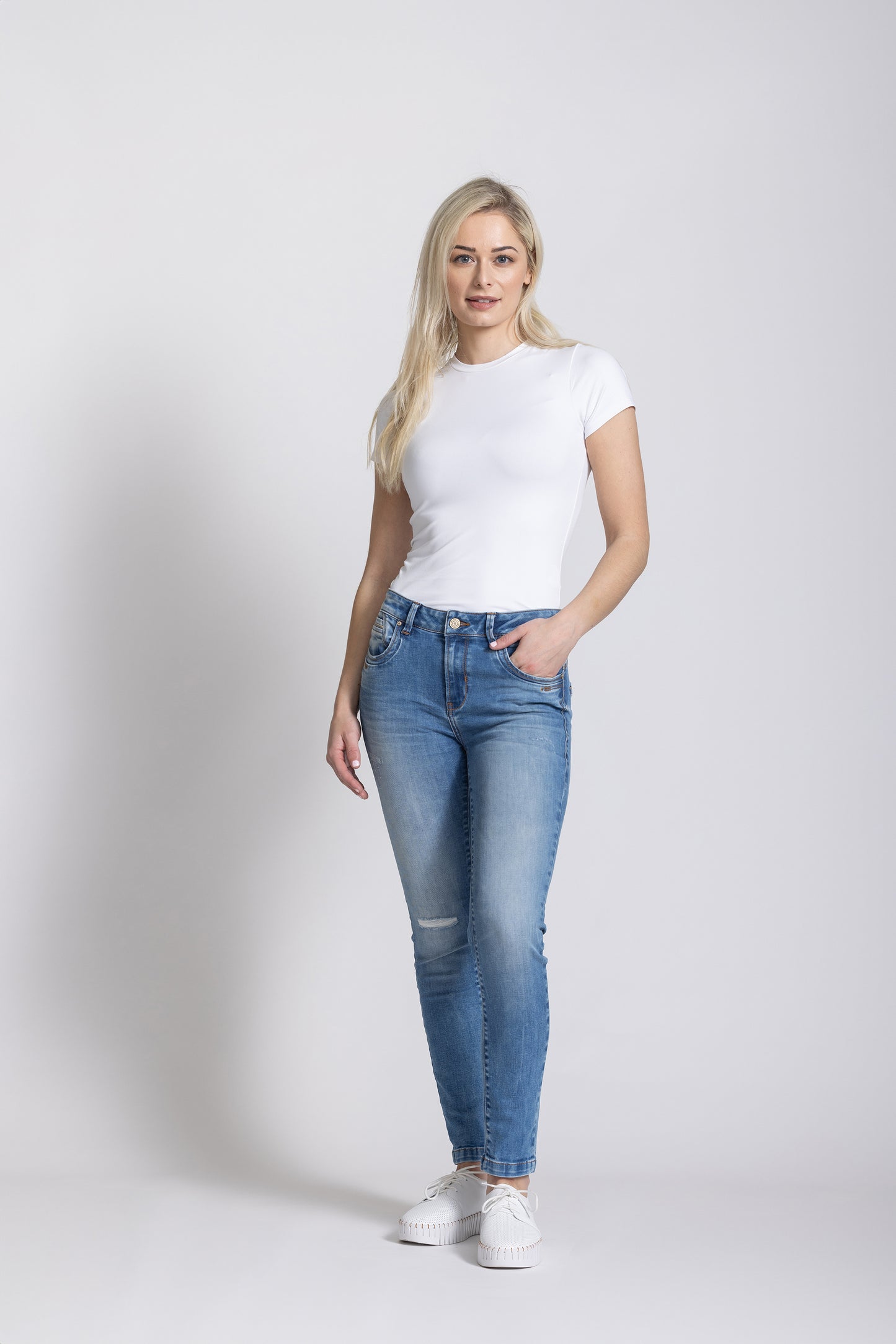 Woman wearing a white t-shirt and blue jeans on a plain background