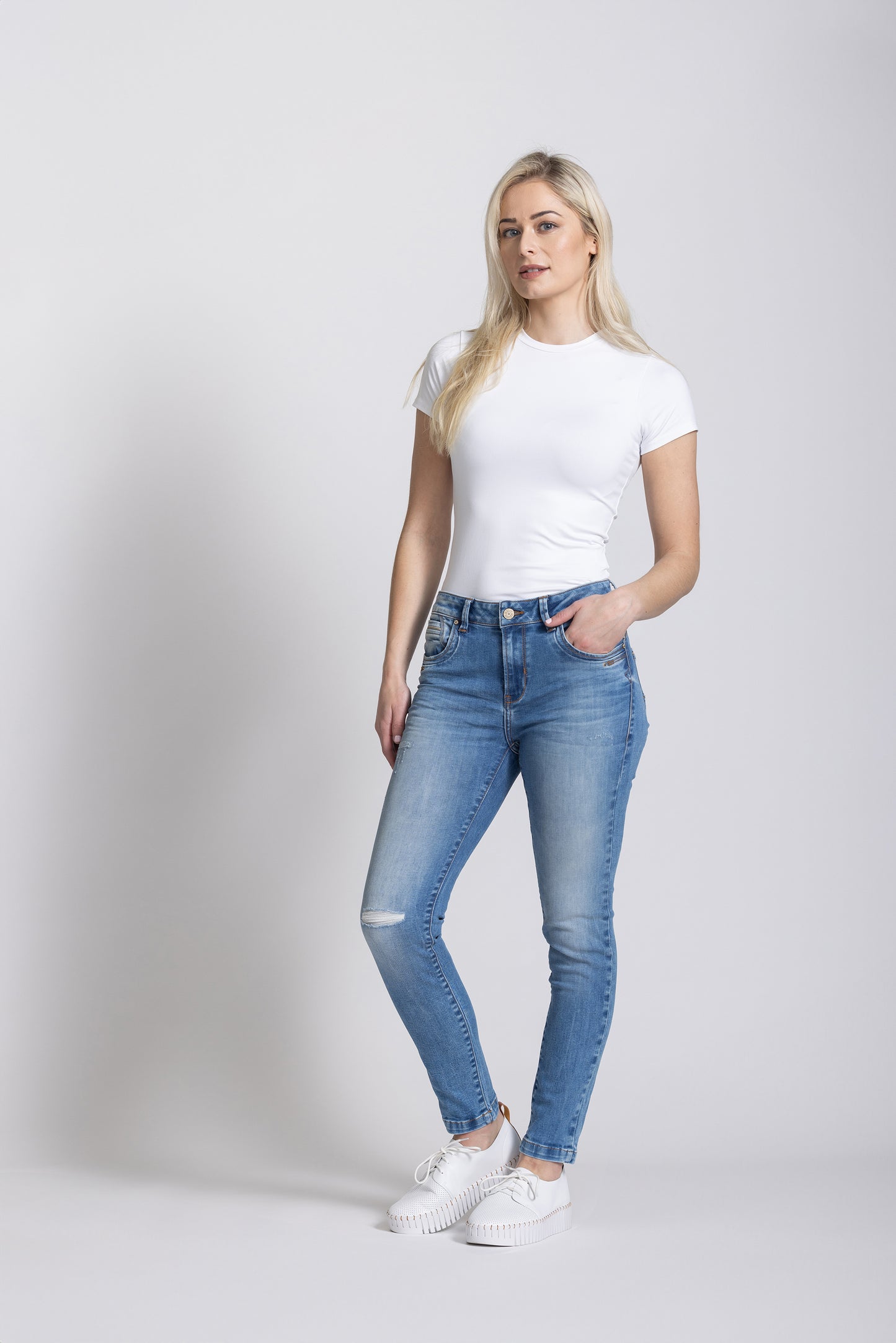 Woman wearing a white t-shirt and light blue jeans on a plain background