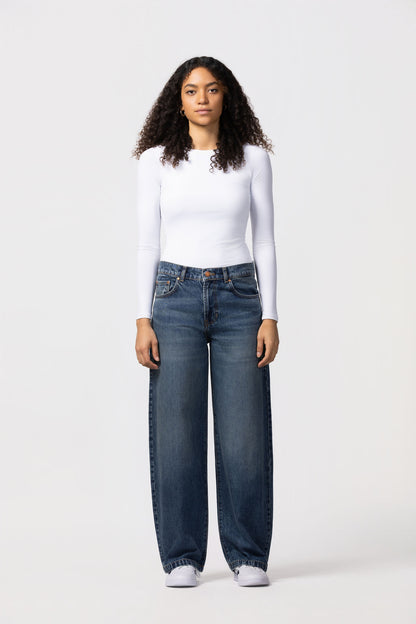 Person wearing a white long-sleeve top and blue jeans on a white background