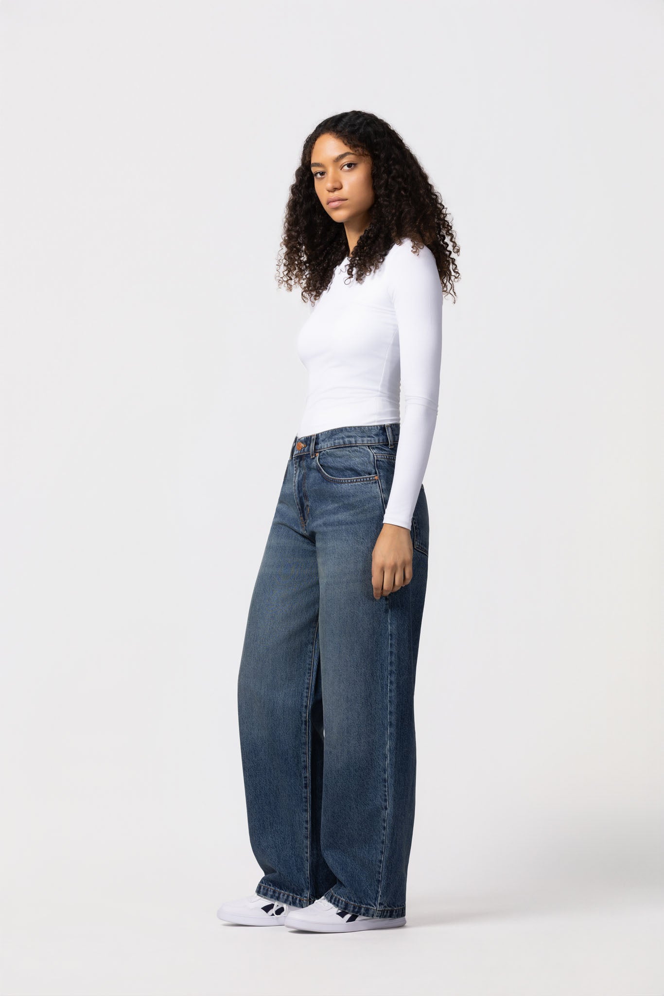 Woman wearing a white long-sleeve top and blue jeans on a white background