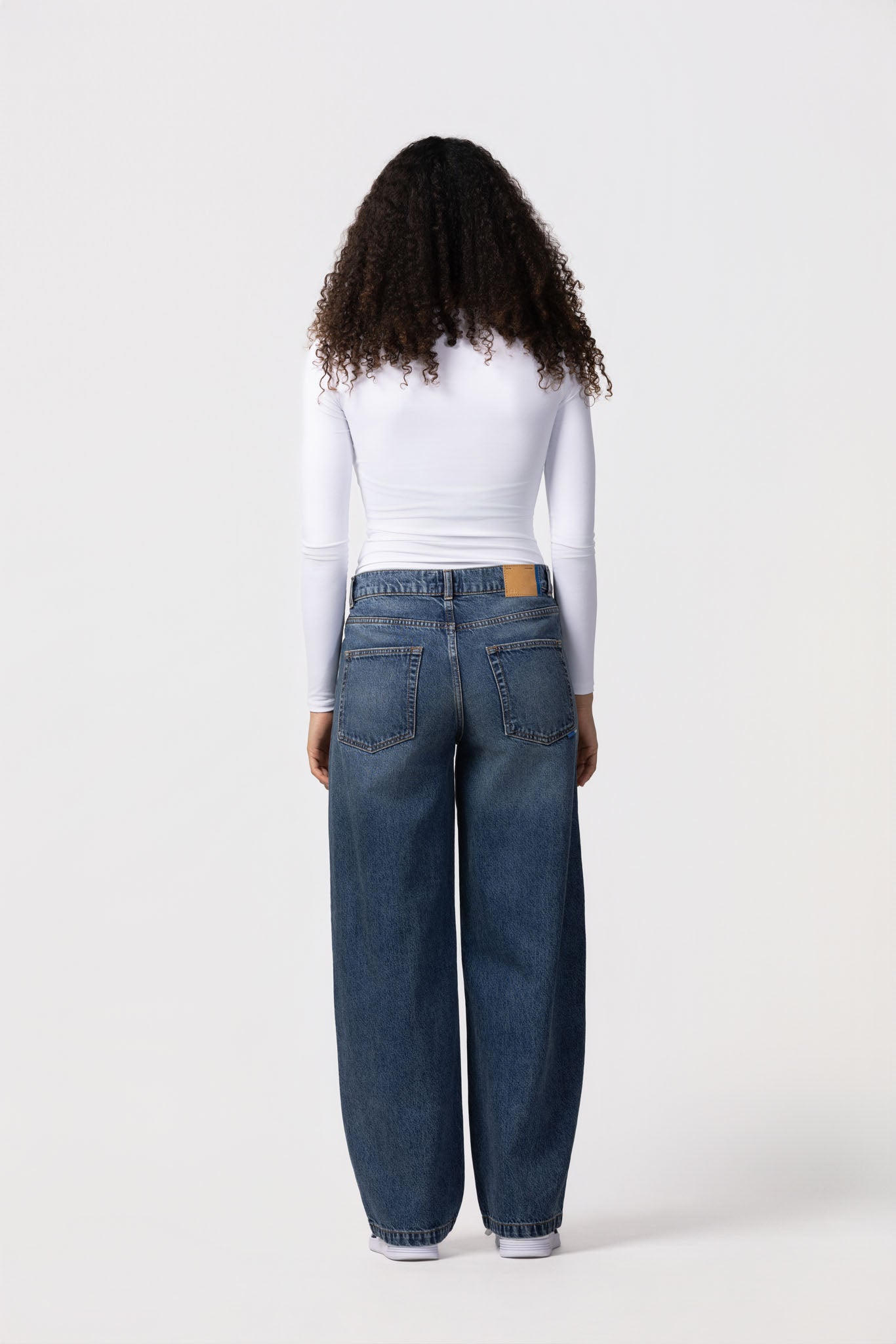 Person wearing blue jeans and a white long-sleeve shirt on a white background