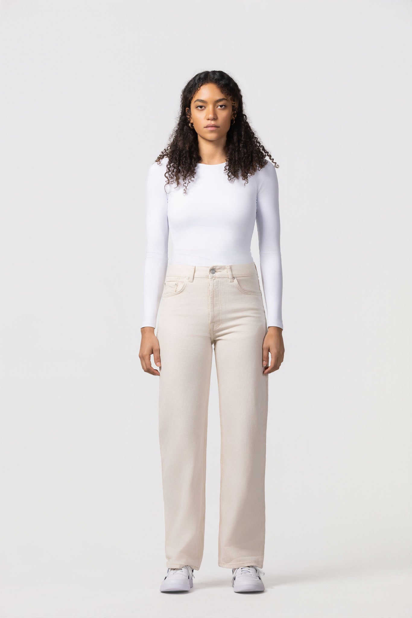 Woman wearing a white long-sleeve top and beige pants on a white background