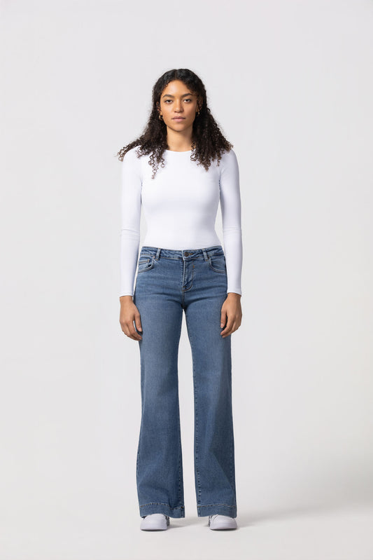 Person wearing a white long-sleeve top and blue jeans on a white background
