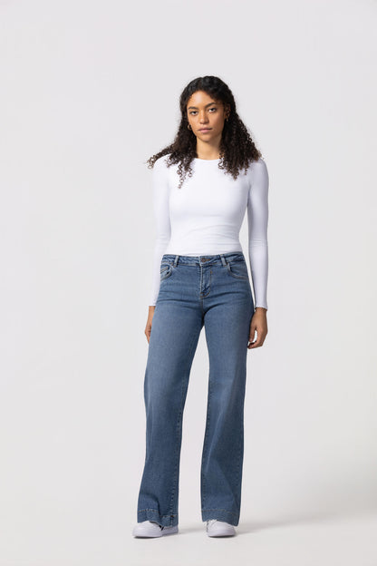 Woman wearing a white long-sleeve top and blue jeans on a white background