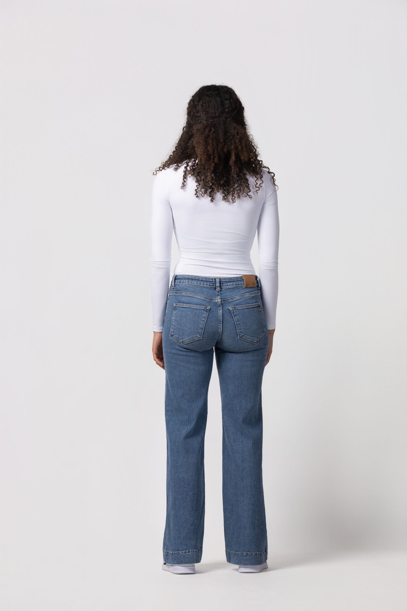 Person wearing blue jeans and a white top on a white background