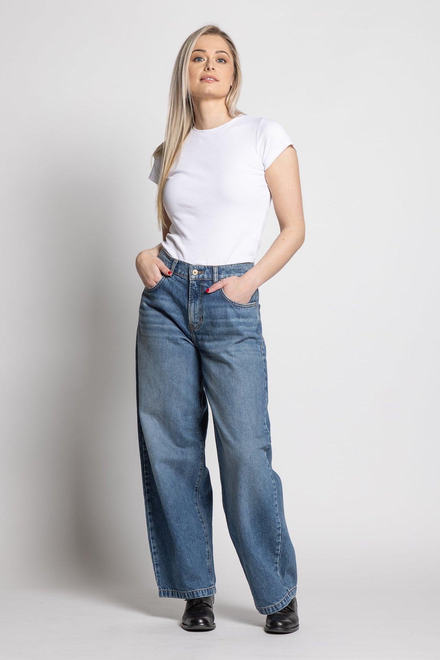 Woman wearing a white t-shirt and blue jeans on a plain background