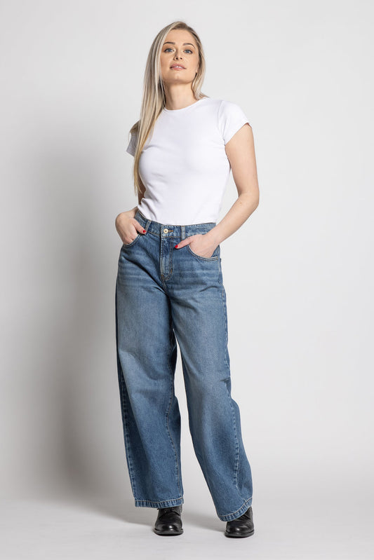 Woman wearing a white t-shirt and blue jeans on a plain background