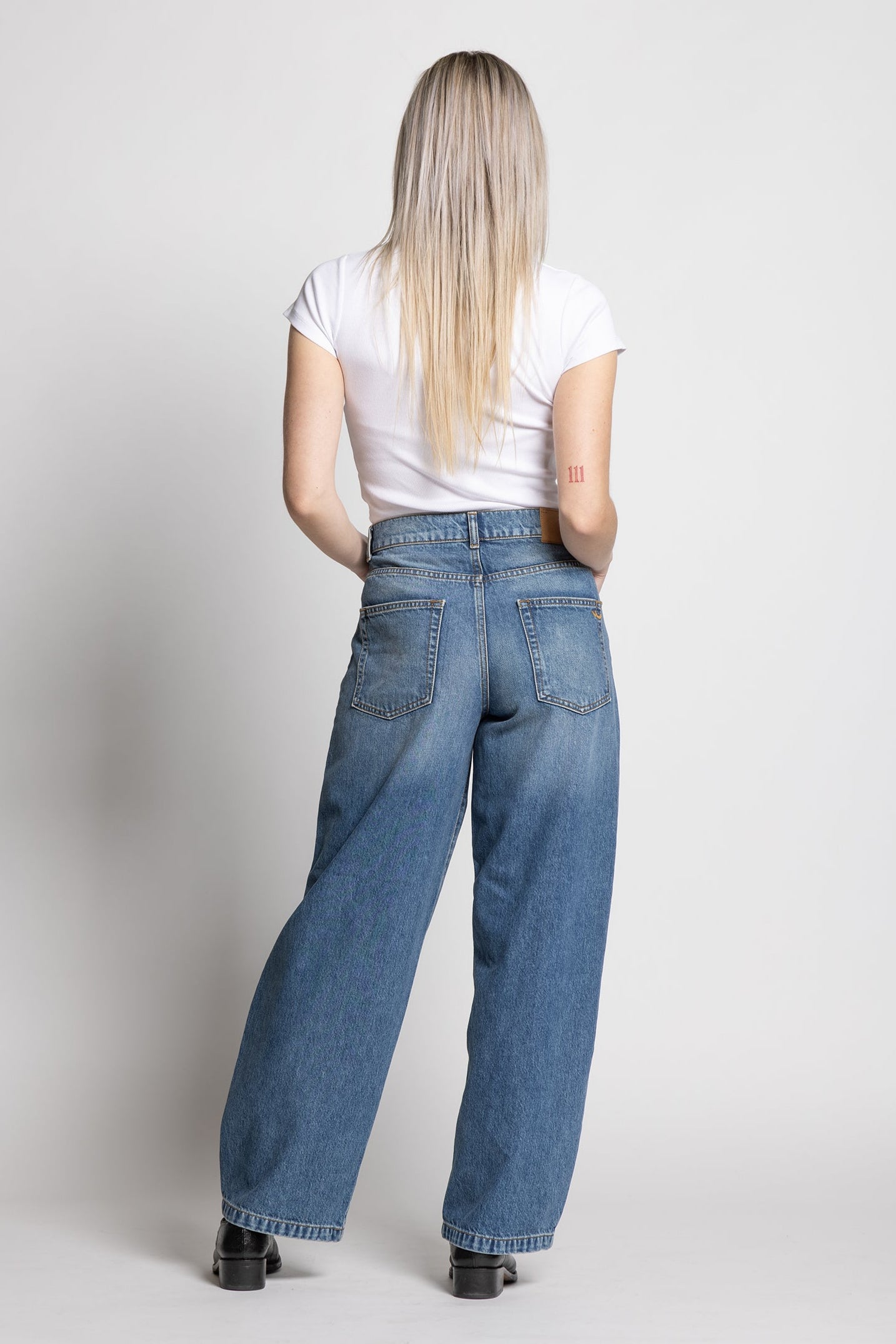 Woman wearing blue jeans and a white shirt on a plain background