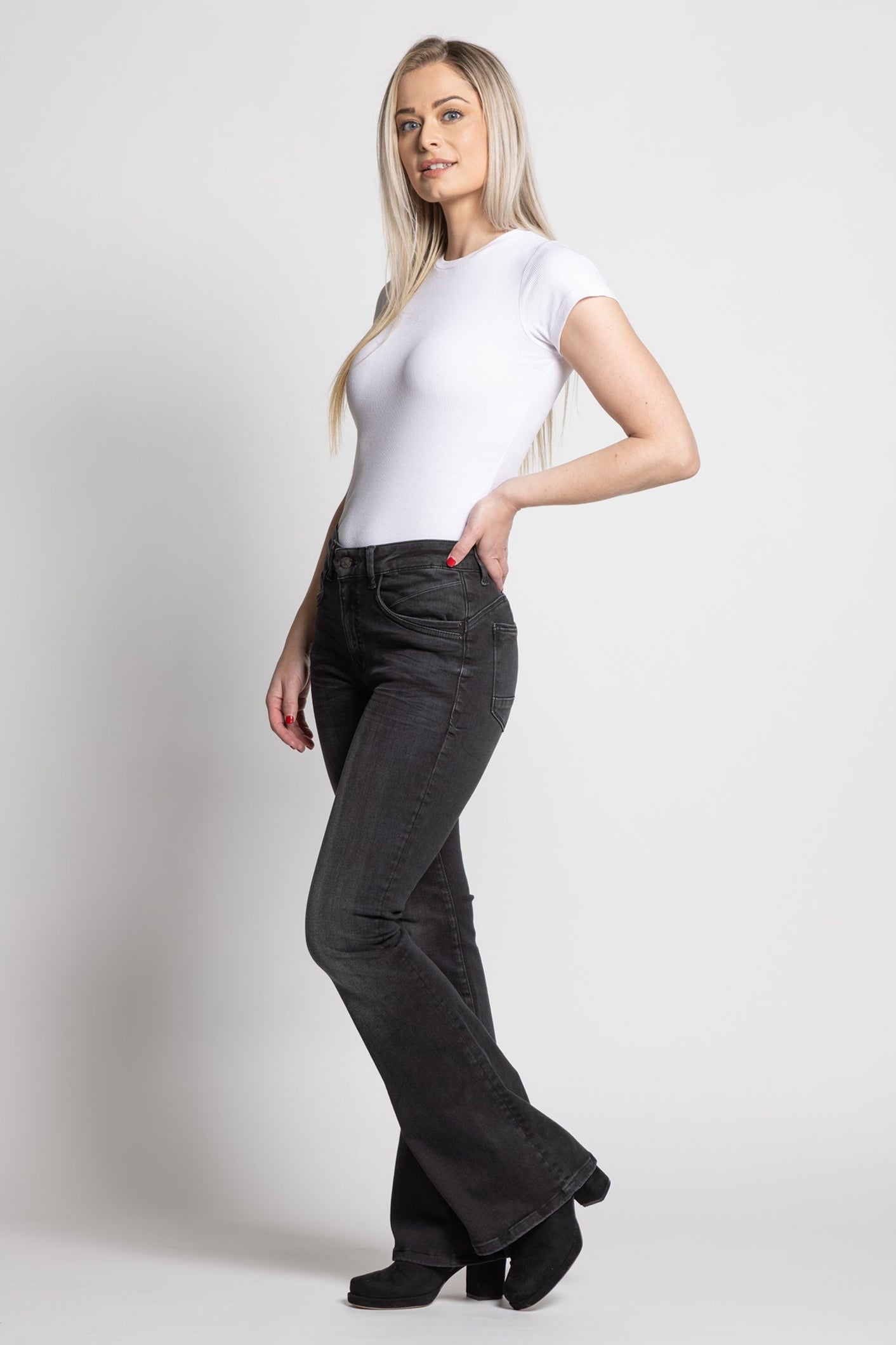 Woman wearing a white t-shirt and dark pants on a plain background