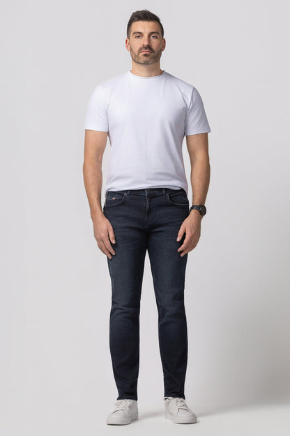 Man wearing a white t-shirt and dark jeans on a plain background