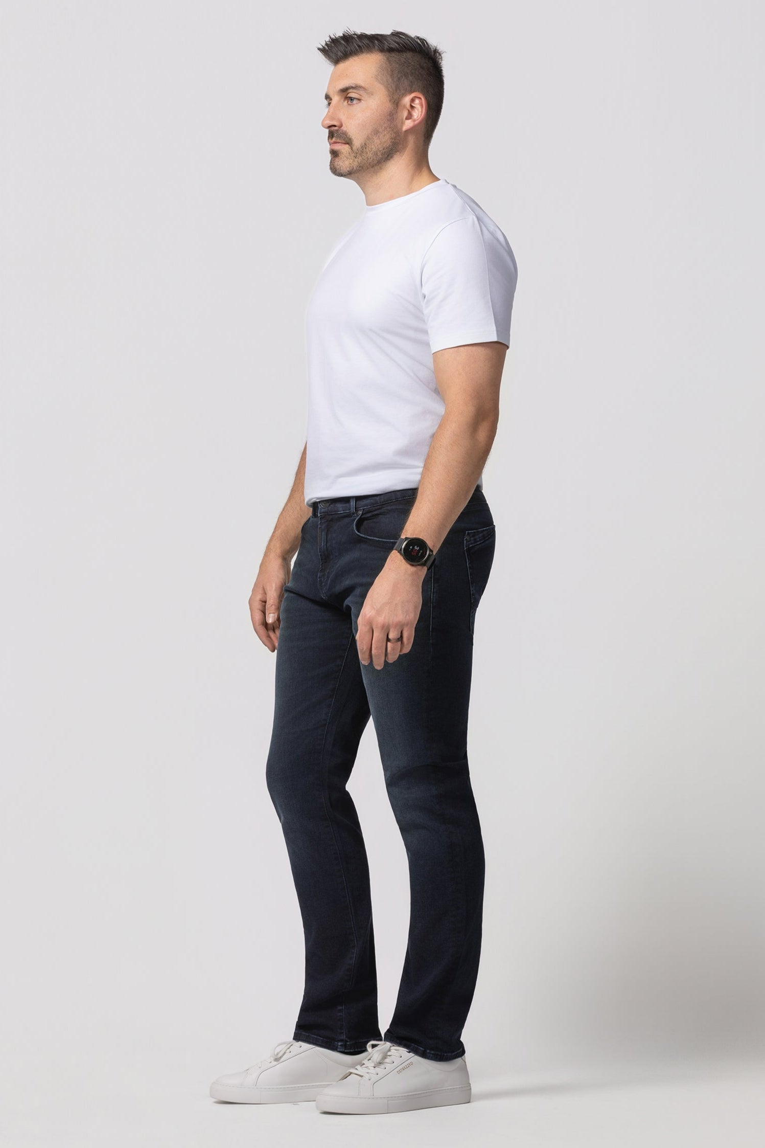 Man wearing a white t-shirt, dark jeans, and white sneakers on a white background