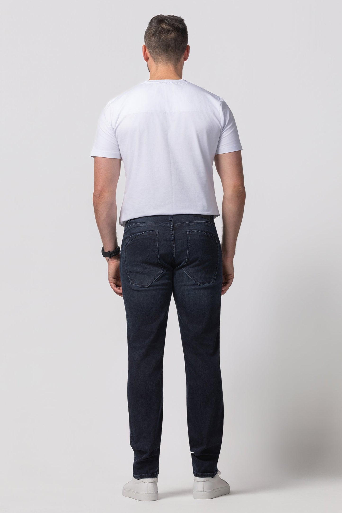 Man wearing a white t-shirt and dark jeans on a plain background