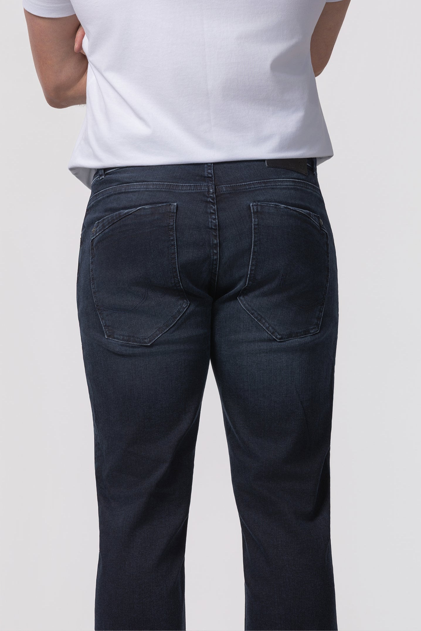 Man wearing dark blue jeans and a white shirt on a plain background