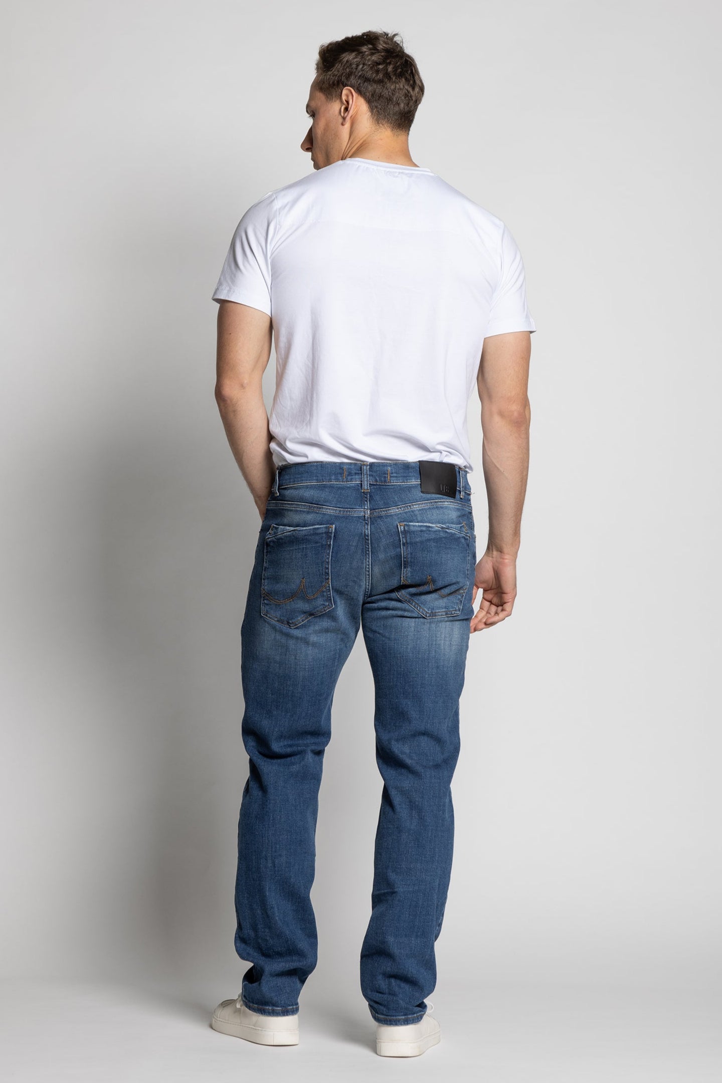 Man wearing a white t-shirt and blue jeans on a plain background