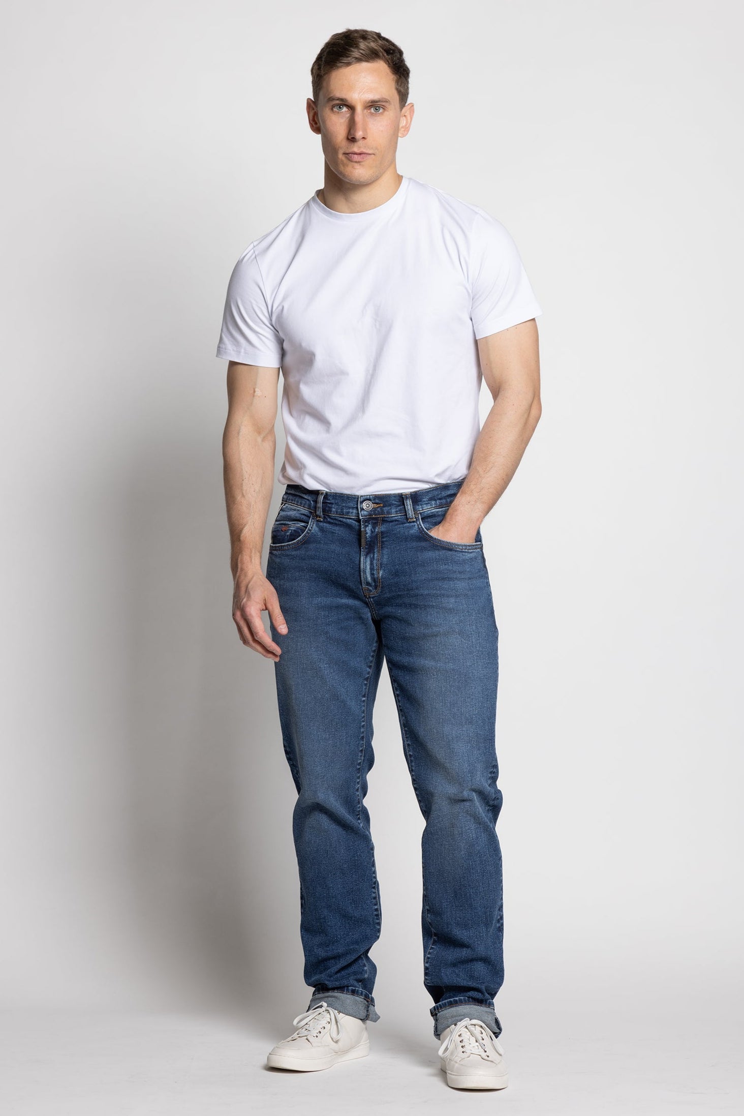 Man wearing a white t-shirt and blue jeans on a plain background