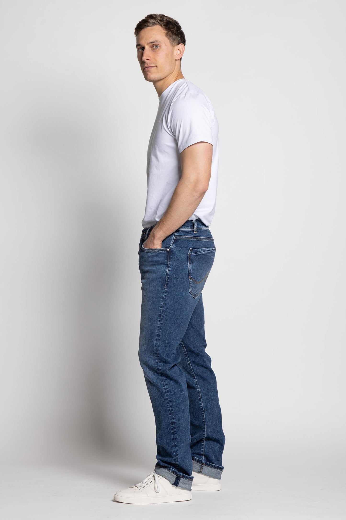 Man wearing a white t-shirt and blue jeans standing against a plain background