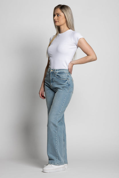 Woman wearing a white t-shirt and light blue jeans on a plain background