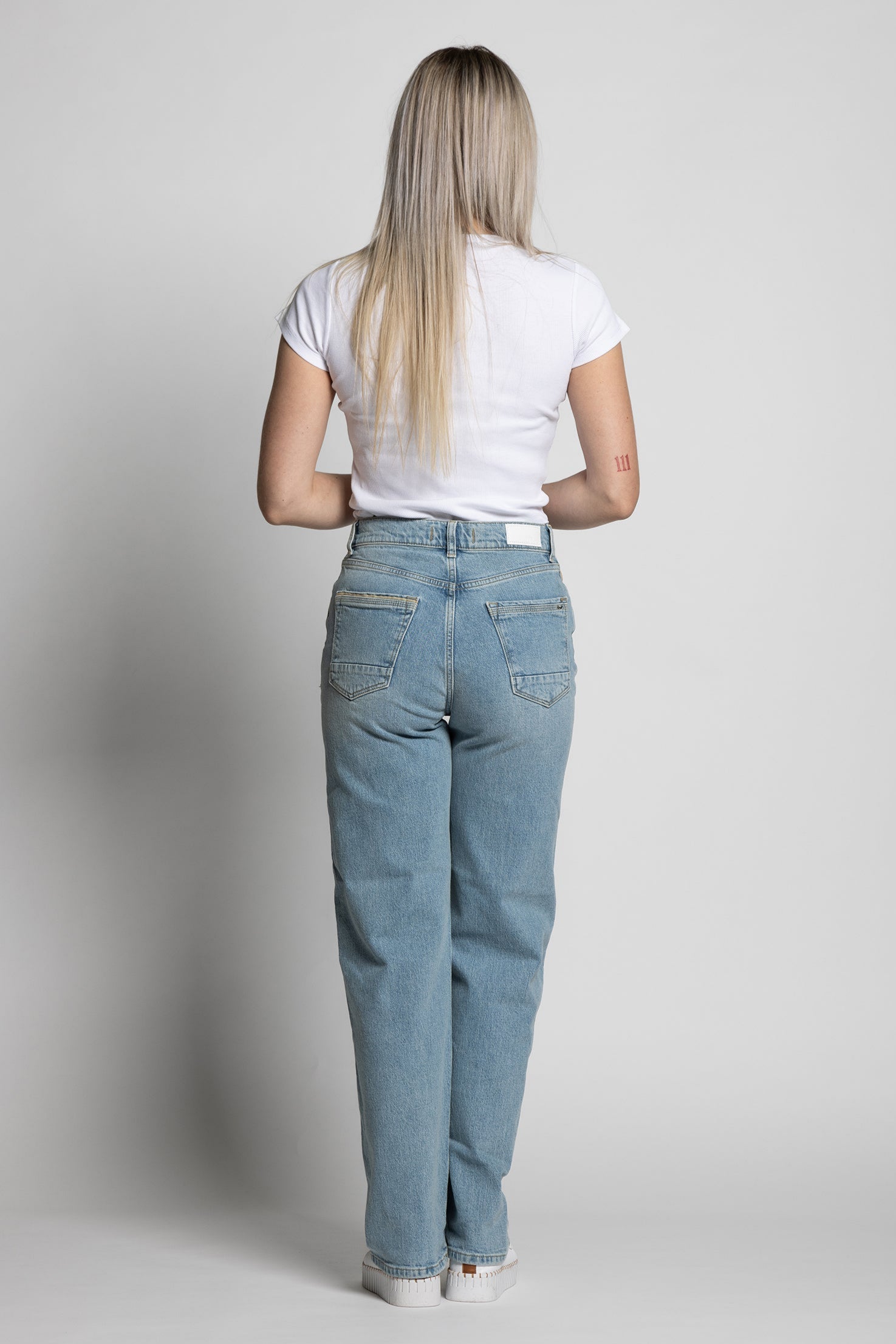 Woman wearing light blue jeans and a white t-shirt on a plain background