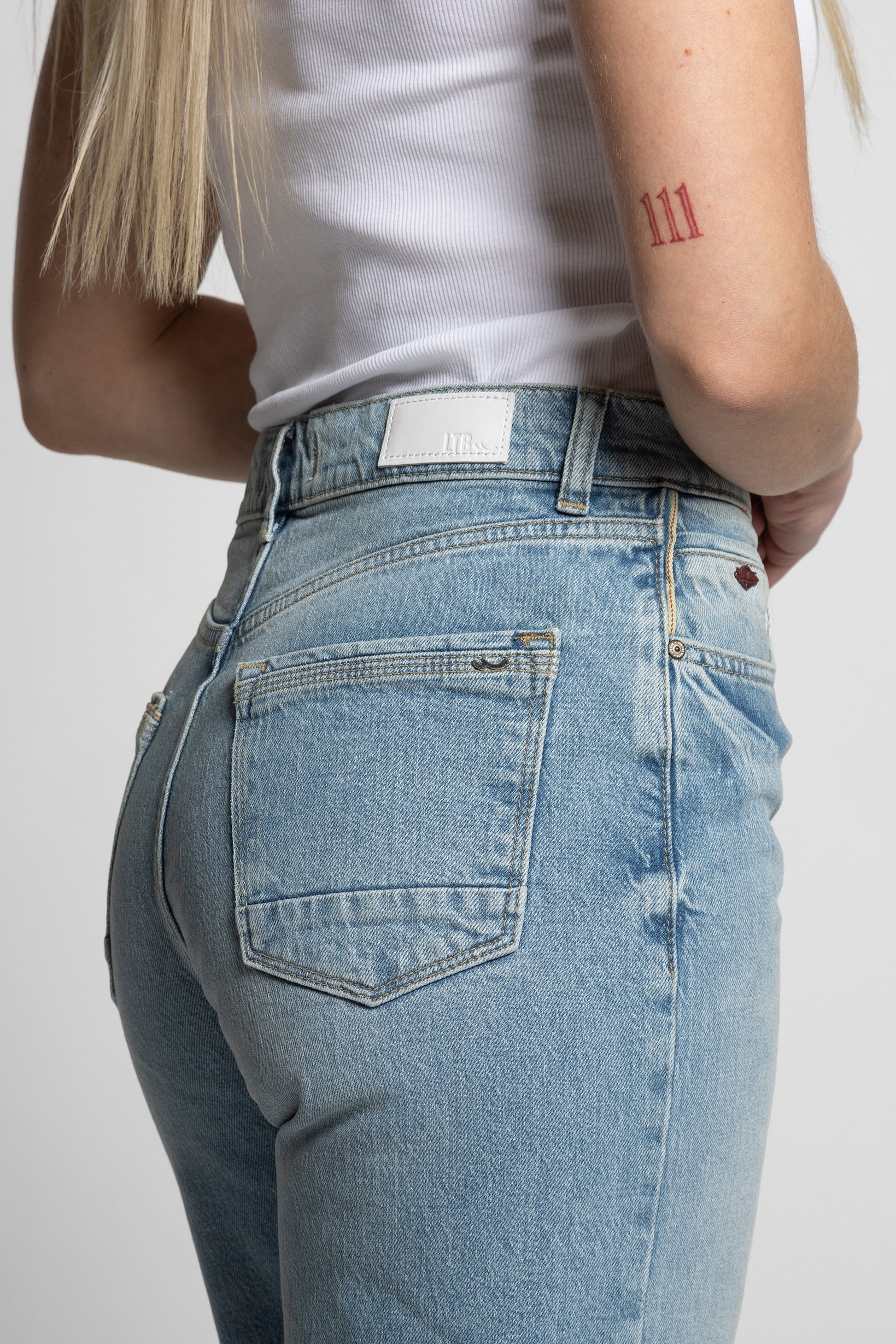 Woman wearing light blue jeans with a white background
