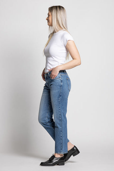 Woman wearing a white t-shirt and blue jeans standing against a plain background