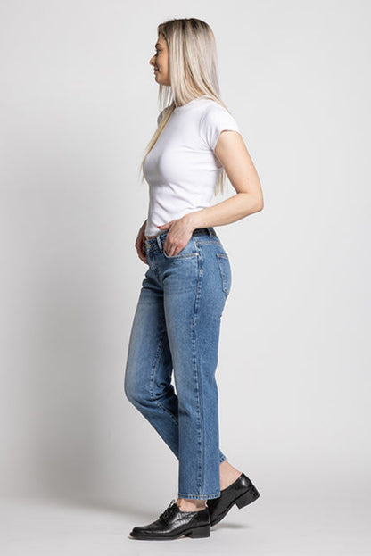 Woman wearing a white t-shirt and blue jeans standing against a plain background